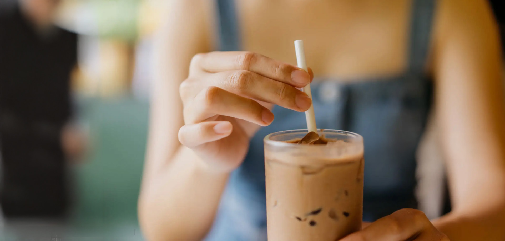 A close up picture of a woman holding a glass with a drink in it and a polymer straw