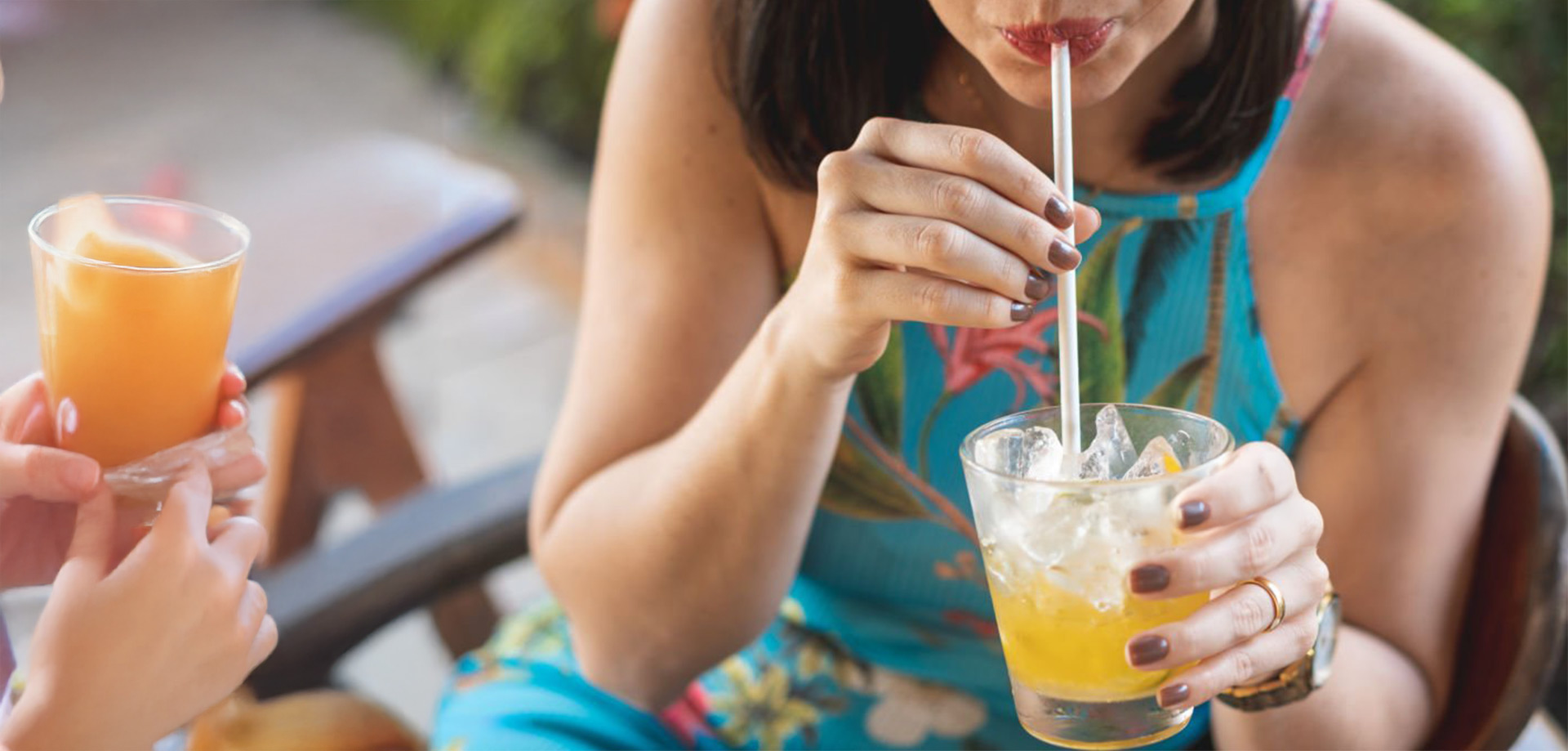 A close up picture of a women wearing a halter dress with short hair sipping through a straw from a glass